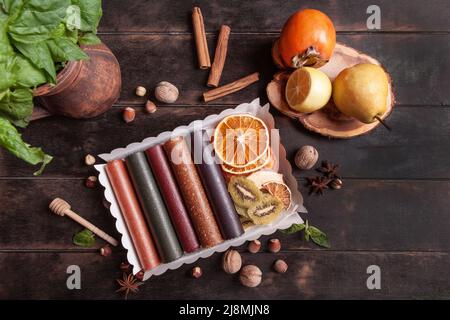 Obstpastilien verschiedener Geschmacksrichtungen und Fruchtchips oder Trockenobstscheiben in einer Geschenkbox, umgeben von frischen Früchten, Nüssen und Gewürzen und frischem Basilikum Stockfoto