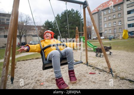 Glückliches kleines Mädchen mit Down-Syndrom auf Schaukel im Freien auf Spielplatz. Stockfoto