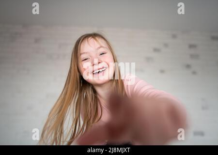 Glückliches kleines Mädchen mit Down-Syndrom, das zu Hause die Kamera anschaut. Stockfoto