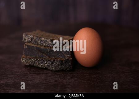 Stücke von schwarzem Brot und ein braunes Ei mit bestreut Salz auf einem dunklen hölzernen Hintergrund Stockfoto