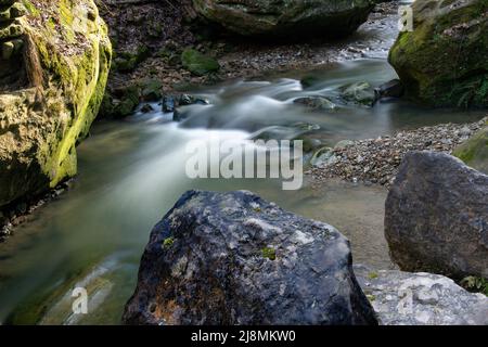 Verschwommenes Wasser fließt zwischen großen Felsen Stockfoto