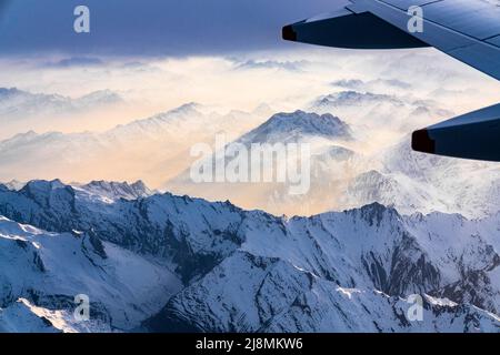 Flugzeug, das während eines nebligen Sonnenuntergangs über Lepontine und Tessiner Alpen fliegt, Kanton Graubünden, Schweiz Stockfoto