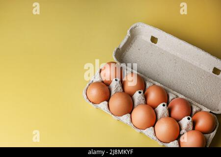 Braune Eier in Öko-Verpackungen aus recycelten Materialien auf einem isolierten hellgelben Hintergrund Stockfoto