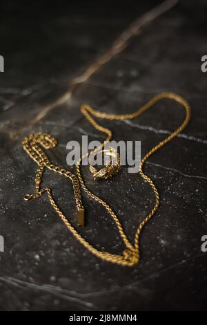 Goldring in Form eines Krokodils mit einer goldenen Kette auf dunklem Marmorboden Stockfoto