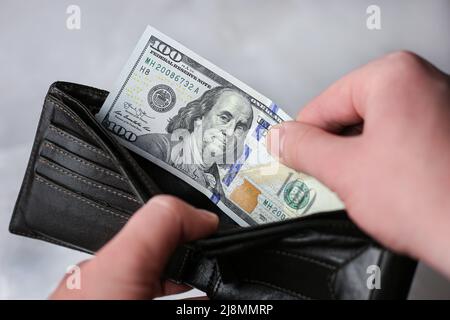 Legt Geldbörse ein oder zieht 100-Dollar-Rechnung heraus Stockfoto