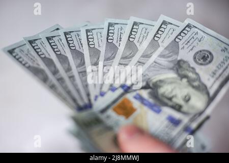 Banknoten von 100 Dollar entfalteten sich in einer Hand auf einem hellen Hintergrund Stockfoto