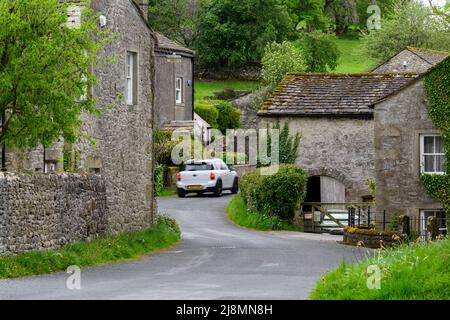 Conistone Village (unberührte attraktive Steingebäude, grüne Felder, steile Talhänge, Auto auf der Straße) - Wharfedale, Yorkshire Dales, England. Stockfoto