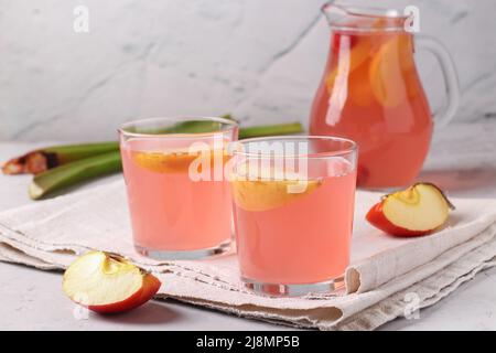 Kompott aus Rhabarber, Äpfeln und Kirschen in zwei Gläsern und einem Krug auf hellgrauem Hintergrund Stockfoto