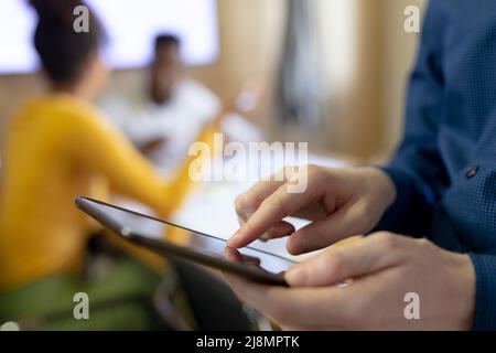 Verkürzte Hände eines afroamerikanischen Geschäftsmannes mit mittlerem Albino-Erwachsenen, der im Büro ein digitales Tablet verwendet Stockfoto