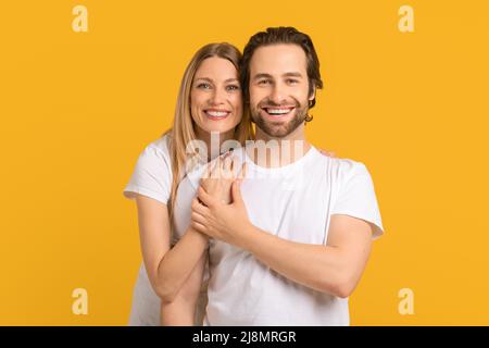 Fröhlich lächelnde junge kaukasische Dame umarmt Mann in weißem T-Shirt schaut auf den Kopierraum Stockfoto