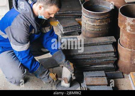 Arbeiter in der Schwerindustrie oder Metallurgie schlagen Eisenplatten mit Hammer ab. Arbeiten Sie mit Metall. Beschaffung von Wertstoffen für die Produktion. Authentischer Workflow. Stockfoto