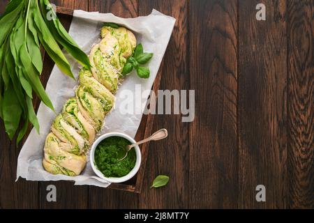 Geflochtenes Bärlauch-Pesto Brioche. Hausgemachtes frisches Pull-Apart-Brot mit Bärlauch-Pesto auf Holzbrett auf Holzhintergrundtisch. Italienisches Brot. C Stockfoto