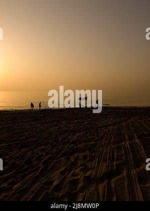 Wunderschöne Aussicht auf den Strand am frühen Morgen mit Fischern in Silhouette ziehen ihre Netze vom Strand in den Ozean. Stockfoto