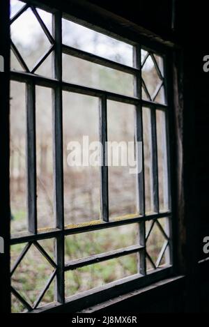 Das alte Fenster mit den alten beschädigten hölzernen Fensterläden an der Wand des alten russischen Hauses Stockfoto