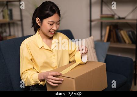 Glücklich asiatische Frau Verpackung Paket mit Klebeband Stockfoto