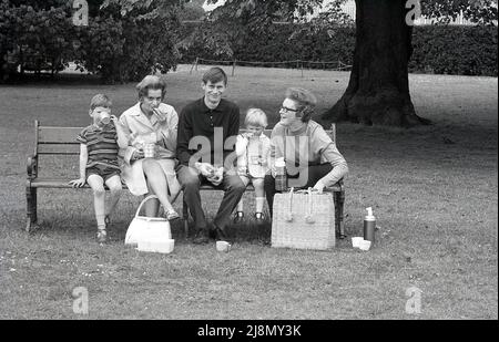 1970s, historisch, eine Familie, die auf einer Parkbank bei einem Picknick sitzt, England, Großbritannien. Stockfoto