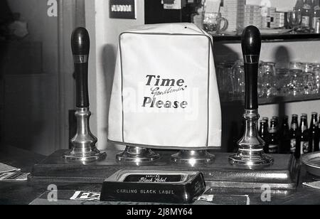 1970s, historisch, eine Haube oder Abdeckung über einer echten Ale Bar Pumpe, England, Großbritannien. Aschenbecher mit Carling Black Label Branding auf der Theke. Stockfoto