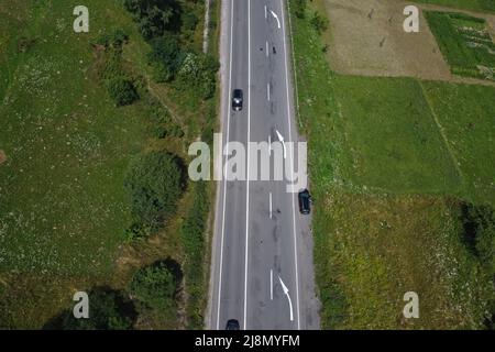 Luftaufnahme von Drohne der Autobahn mit drei Spuren zwischen grünen Feldern direkt darüber. Asphaltierte Straße mit gebrochenen weißen Linie Straßenmarkierungen Stockfoto