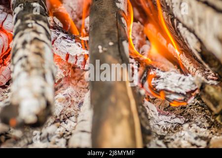 Eine Nahaufnahme von Holzstücken und Brennholz, Holzkohle und Asche, die in Flammen brennen. Stockfoto