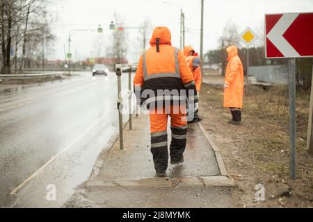 Arbeiter auf der Straße. Straßenarbeiter säubern Müll. Menschen in orangefarbenen Kleidern. Der Verkehrsdienst unterhält die Seite der Autobahn. Stockfoto