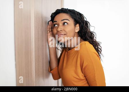 Nosy African Female, Die Im Innen Ohr An Die Tür Legt Und Klatsch Hört Stockfoto