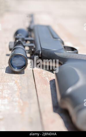 Ein Scharfschützengewehr mit optischer Sicht liegt auf einem abgenutzten Holzbrett. Waffe mit optischem Blick. Waffenlieferungen. Selektiver Fokus. Stockfoto