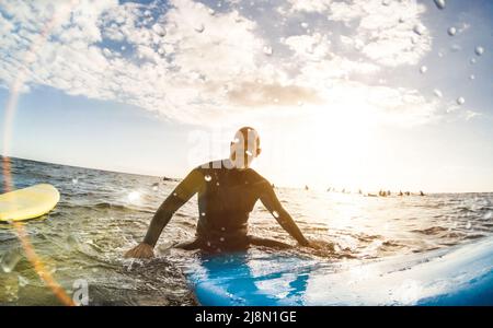 Guy Surfer beim Sonnenuntergang auf Teneriffa auf Surfbrett relaxen mit unkenntlichen Leuten auf Surfbrettern im Hintergrund - Sportreisekonzept Stockfoto