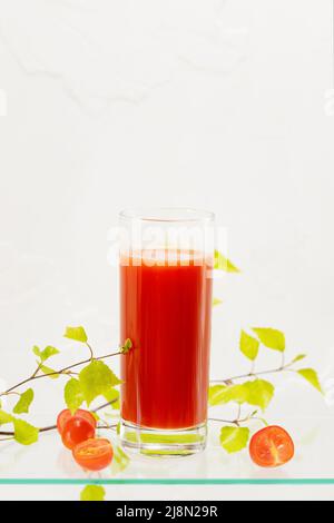 Glas natürlichen Tomatensaft mit frischen Kirschtomaten und grünem Zweig auf einem Glasregal auf weißem Hintergrund mit Kopierfläche. Gesunde Jahreszeit vega Stockfoto