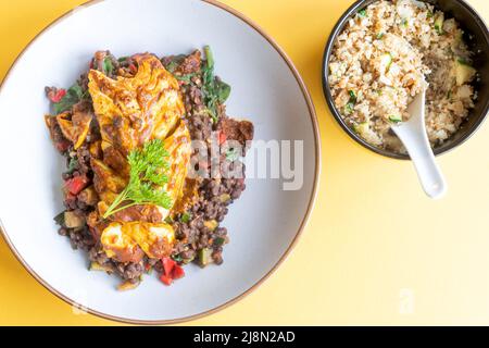 Ein frischer Kabeljau, mariniert in Tikka-Limonade, serviert auf einem Bett aus puy-Linsen, gemischt mit Spinat und serviert mit einer Seite Blumenkohlreis Stockfoto