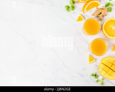 Mango-Orangensaft-Smoothie in Gläsern auf weißem Marmorboden. Frisches, gesundes Getränk. Draufsicht, Kopierbereich, flach liegend Stockfoto