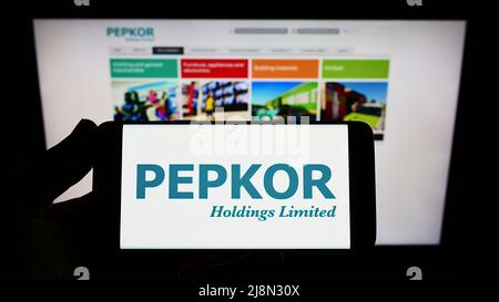 Person, die das Smartphone mit dem Logo des südafrikanischen Unternehmens Pepkor Holdings Limited auf dem Bildschirm vor der Website hält. Konzentrieren Sie sich auf die Telefonanzeige. Stockfoto