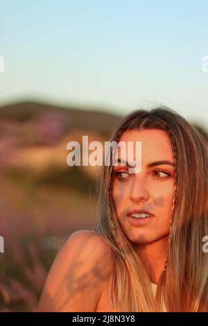 Porträt einer jungen Frau mit Schatten von Lavendelblüten auf ihrem Gesicht bei Sonnenuntergang in einem Lavendelfeld und Blick auf eine Seite Stockfoto