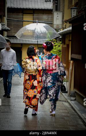 Zwei Mädchen, die einen Kimono tragen, gehen die Straße entlang Stockfoto