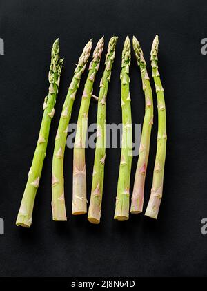 Sieben Spargelspieße sind auf schwarzem Hintergrund angelegt. Stockfoto