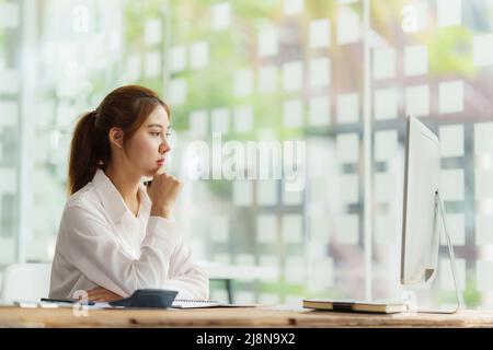 Schöne asiatische Geschäftsfrau, die sich ein informatisches Webinar am Computer ansieht. Finanzierungskonzept. Stockfoto