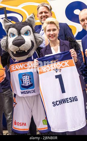 Schwerin, Deutschland. 17.. Mai 2022. Manuela Schwesig (SPD, M), die Ministerpräsidentin von Mecklenburg-Vorpommern, hält ihr neues Trikot mit der Nummer 1 zwischen den Vorstandsmitgliedern Jens Hakanowitz (l) und André Jürgens (r) und den Basketballspielern der Rostock Seawolves. Mit ihrem Eintritt in das Playoff-Finale der 2. Liga ProA, die Mecklenburger Seenplatte hatten letzte Woche ihre erste Beförderung zum deutschen Basketball-Spitzenflug Perfect gemacht. Quelle: Jens Büttner/dpa/Alamy Live News Stockfoto