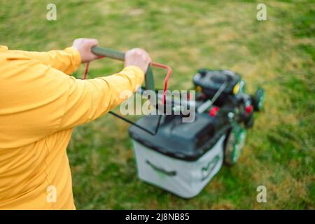 Rasenmähen mit einem Rasenmäher im Frühjahr oder Sommer. Gärtnerin schneidet den Rasen im Garten. Arbeiter mäht hohes Gras mit elektrischem oder Stockfoto