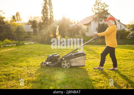 Junge Frau schneidet Gras mit einem Rasenmäher. Konzept der Hausarbeit im Freien. Stockfoto