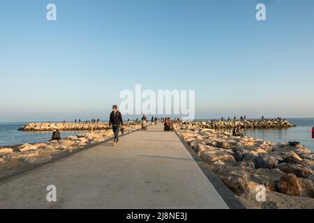 Menschen, die bei Sonnenuntergang auf einem Steinpier spazieren, Fuengirola, Andalusien, Costa del sol, Spanien. Stockfoto