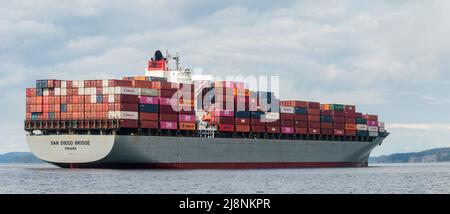 Ein Blick auf Wasserhöhe auf das riesige, beladene Containerschiff San Diego Bridge, das auf den Gulf Islands von British Columbia vor Anker lag, während es auf den Zugang zum Hafen von Vancouver wartete. Stockfoto