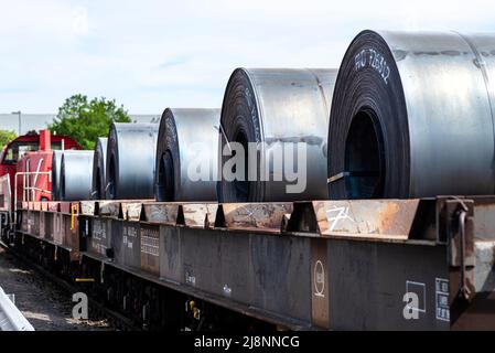 Große Blechrollen liegen auf einem von Lokomotiven gezogenen Güterwagen. Stockfoto