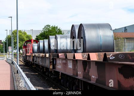Große Blechrollen liegen auf einem von Lokomotiven gezogenen Güterwagen. Stockfoto