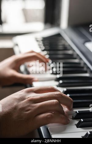 Detailansicht der Hände eines jungen dunkelhaarigen Mannes, der auf elektronischem Klavier oder Synthesizer spielt. Latin-Mann, der sein Hobby zu Hause praktiziert Stockfoto