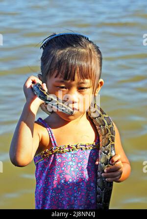 Siem Reap, Kambodscha - Dezember 9. 2019: Porträt des armen khmer kambodschanischen Mädchens, das konzentriert mit ihrer Pythonschlange um den Hals am Fluss posiert Stockfoto