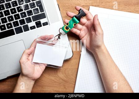 Auf einem Notebook und einem Laptop halten die Hände einer jungen, nicht erkennbaren Person einen leeren Personalausweis mit einem Trageband aus Sonnenblumen, Symbol für Menschen mit invisibl Stockfoto