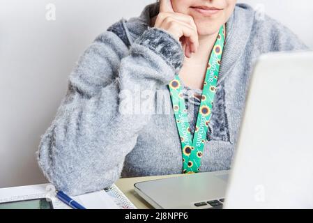 Eine unkenntliche Frau schaut auf einen Laptop, studiert oder arbeitet zu Hause und benutzt dabei ein Sonnenblumenklederband, das Symbol für Menschen mit unsichtbarem oder verstecktem DIS Stockfoto