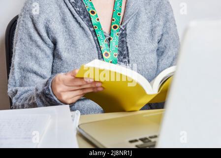 Nicht erkennbare Frau, die ein gelbes Buch liest, zu Hause studiert oder arbeitet, mit einem Sonnenblumenklederband, Symbol für Menschen mit unsichtbaren oder versteckten Disabili Stockfoto