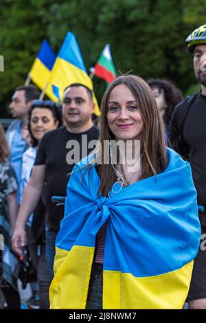 Sofia, Bulgarien - 09. Mai 2022: Ein lächelndes Mädchen, in ukrainische Flagge gehüllt, geht in einer Menschenmenge bei der Support Ukraine Demonstration Stockfoto