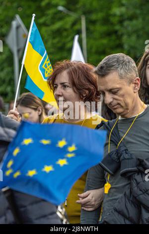 Eine Frau mittleren Alters geht in einer Menschenmenge mit einer mittelgroßen ukrainischen Flagge, die in ihrer Hand angehoben ist, und der Flagge der Europäischen Union vor ihr Stockfoto