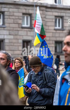 Ein Mann auf der Straße hält Flaggen der Ukraine, Bulgariens und der EU und schaut in seinem Smartphone auf den Support Ukraine march Stockfoto